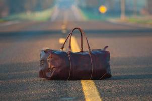 Brown leather duffel bag in middle of asphalt road photo