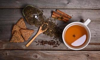 Cup of green tea, cookies and cinnamon on wooden background photo