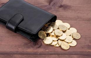 Black leather wallet with golden coins on wood background