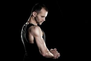 muscular man,  clasps hands in  fist, black background, place for photo