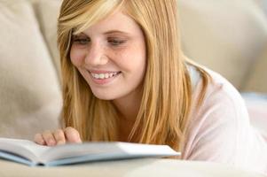 Smiling student teenager reading book on sofa