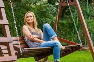 Sensual blonde woman sitting in park on wooden bench. Outdoor