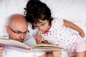 father and daughter reading a book in bed photo