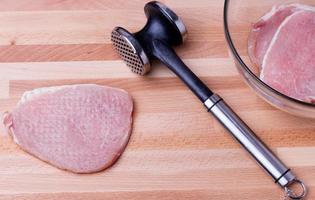 Raw pork schnitzel with meat tenderizer on wooden board photo