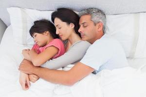 padres durmiendo con su hija en la cama foto