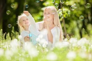 Happy mother and daughter blowing bubbles in the park photo