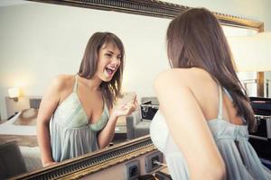 Cheerful young woman in front of mirror applying make-up photo