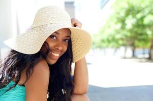 Feliz joven mujer negra sonriendo con sombrero para el sol al aire libre