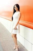 Beautiful young woman in white dress with handbag clutch outdoor photo