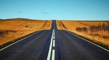 Carretera de asfalto negro entre campos marrones foto