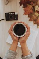 Person holding coffee cup with camera and notebook on table photo