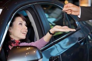 Mujer joven recibiendo las llaves del coche del vendedor de coches foto