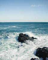 Ocean waves crashing on rocks under a blue sky photo