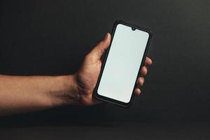 mano joven sosteniendo un teléfono con una pantalla blanca foto