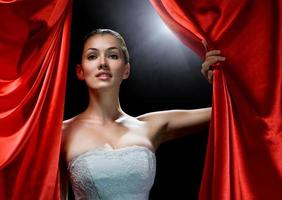 A young woman coming from behind red curtains photo