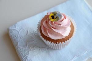 Homemade pink frosting vanilla cupcakes with edible flowers photo