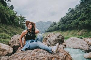 mujer feliz, reír, mientras, sentado, en, el, roca, por, río foto