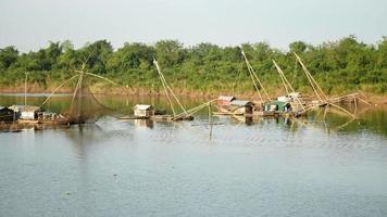 casas flutuantes e redes de pesca chinesas no rio; pescador levantando rede de pesca chinesa da água