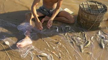 pescador removendo peixes emaranhados e mantendo-os em uma cesta de bambu