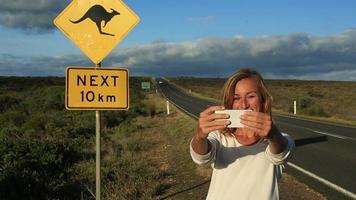 jovem viajando tira selfie com placa de cruzamento de canguru