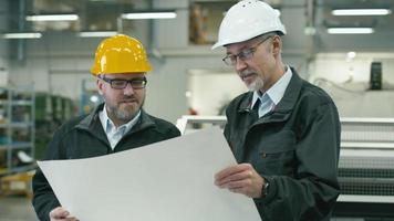 två ingenjörer diskuterar en ritning medan de kontrollerar informationen på en surfplatta i en fabrik.
