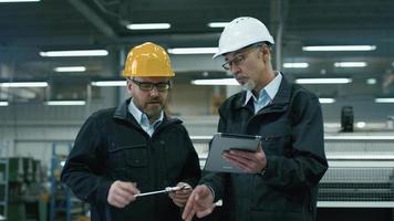 dois engenheiros discutem um projeto enquanto verificam as informações em um tablet em uma fábrica.
