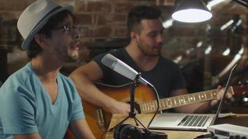 Dos jóvenes cantan y tocan la guitarra mientras graban una canción en un estudio casero en un garaje.