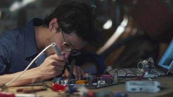 estudiante estudia electrónica y suelda una placa de circuito en un garaje. video