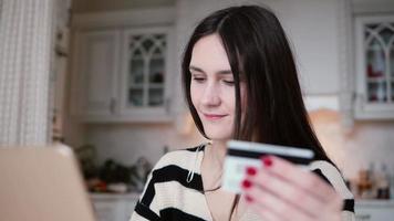aantrekkelijke jonge lachende vrouw maakt gebruik van plastic creditcard online winkelen met laptop video