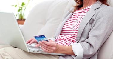 Mujer sonriente con una tarjeta de crédito y un portátil en un sofá