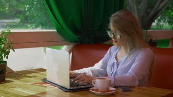 Mujer de negocios con gafas trabajando en la cafetería y hablando por teléfono inteligente.