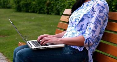 donna seduta su una panchina nel parco utilizzando il computer portatile