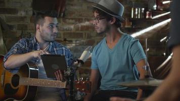 banda de músicos discutem em um estúdio de garagem enquanto usam um computador tablet. video
