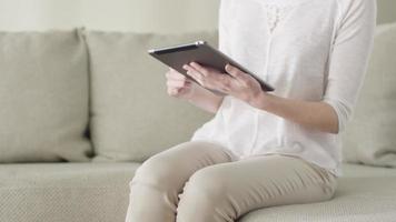 mooie jonge vrouw gebruikt een tabletcomputer zittend op een bank thuis. video
