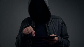 Criminoso cibernético encapuzado irreconhecível com computador tablet digital video