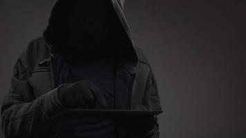 Unrecognizable hooded cyber criminal with digital tablet computer