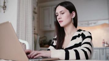 portret van een mooie jonge brunette vrouw gebruikt laptop in een lichte eetkamer video