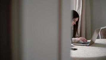 donna utilizza il computer portatile e godersi il caffè del mattino in una sala da pranzo luminosa. cursore a destra, vista attraverso le porte aperte video