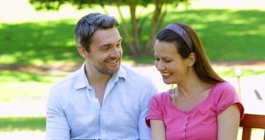 Happy couple sitting on a park bench using tablet pc