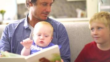 moderner Vater liest seinen Kindern auf der Couch ein Buch vor