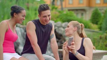 Multiracial people having fun using phone in park. Young friends laughing video
