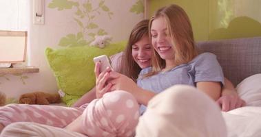 adolescente meisjes die een telefoon gebruiken terwijl ze samen in bed liggen