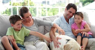 Linda familia relajándose juntos en el sofá con su perro video