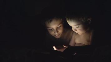 Two young brothers playing with tablet at night. 4K