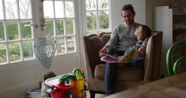 padre si siede sulla sedia a casa leggendo un libro al figlio girato su r3d