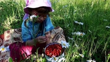 niña come fresas silvestres en el prado. video