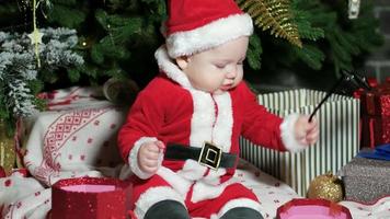 Babbo Natale ragazzino, bambino in costume da Babbo Natale, giocando con gli occhiali, bambino si siede nei costumi di carnevale, costumi di Natale sotto l'albero di Natale video