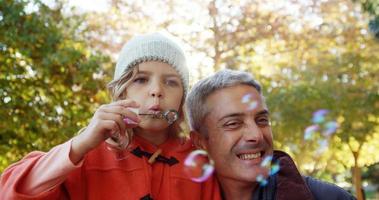 Girl blowing bubbles held by dad outdoors