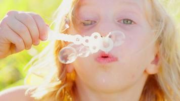 Young blonde girl blowing bubbles outside