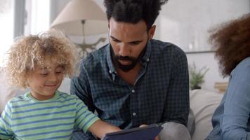 padre e figlio seduti sul divano utilizzando la tavoletta digitale
